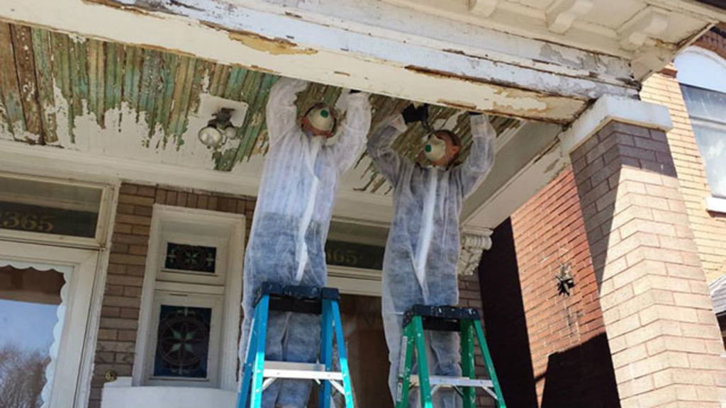 Guys scraping paint off a porch ceiling.
