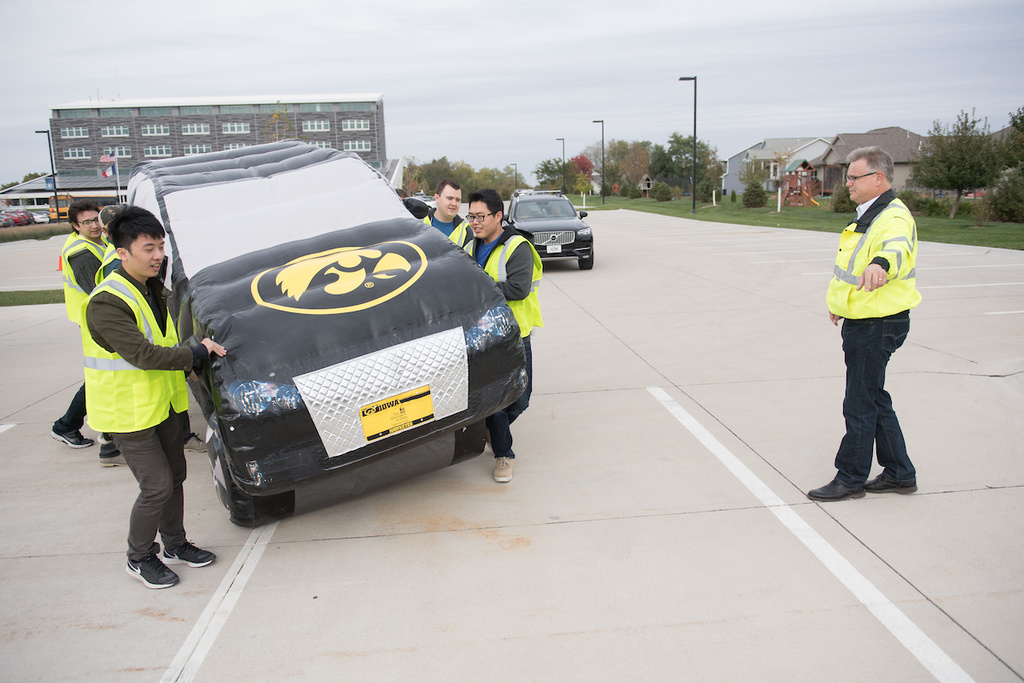 students place inflatable car on parking lot as instructor gives directions