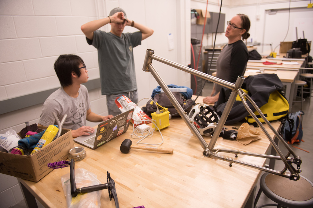bike-building students talk around table that has bike frame atop it