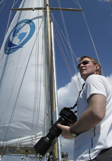 Photo of a man holding a camera in front of a sail on a sailboat