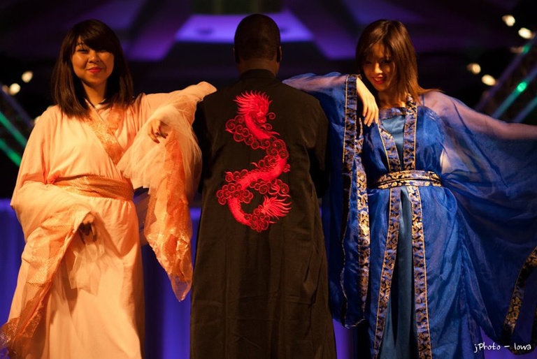 Three models wearing cultural costumes in peach, black and blue