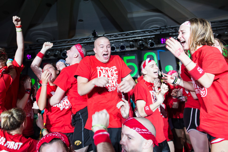 Students in red t-shirts dance and celebrate on a stage