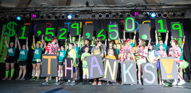 Children hold up signs with the number 1,529,650.19 and the letters T H A N K S on a stage.