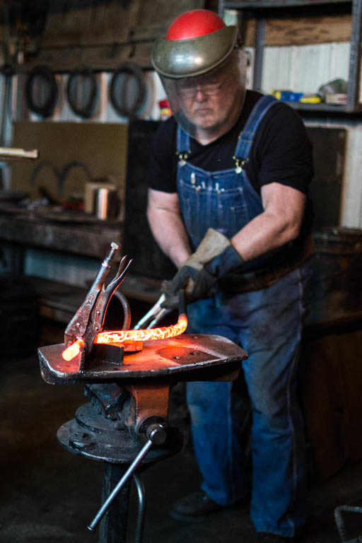 A man bends a red hot rod of steel.