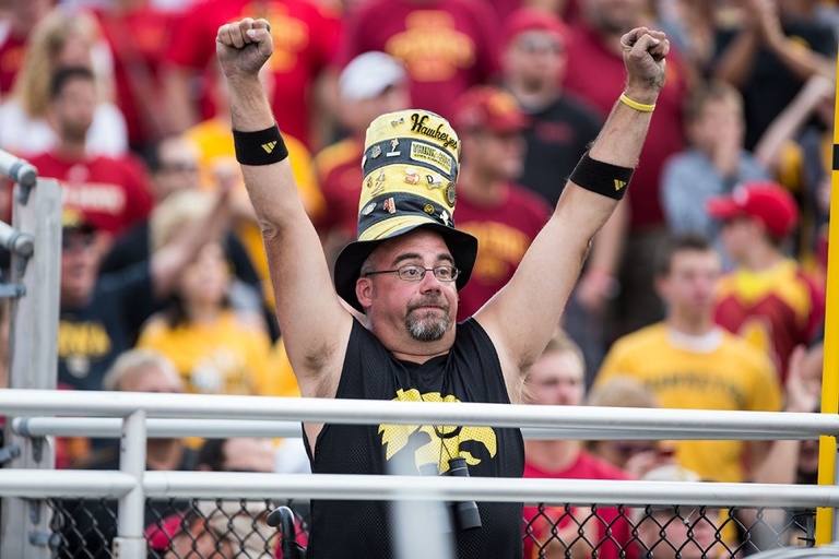 A man in Iowa Hawkeye gear raises his fists in the air in celebration.