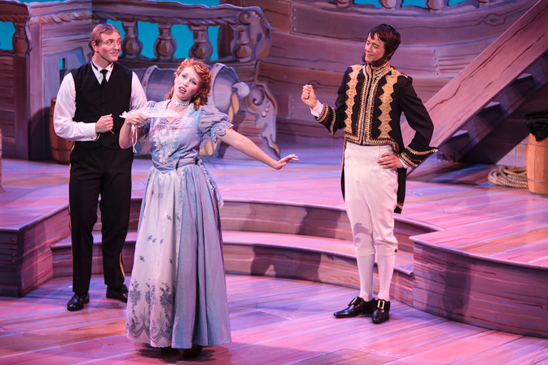 A man dressed as a sea captain, a woman in a dress with a fan, and a man dressed as an admiral sing together.