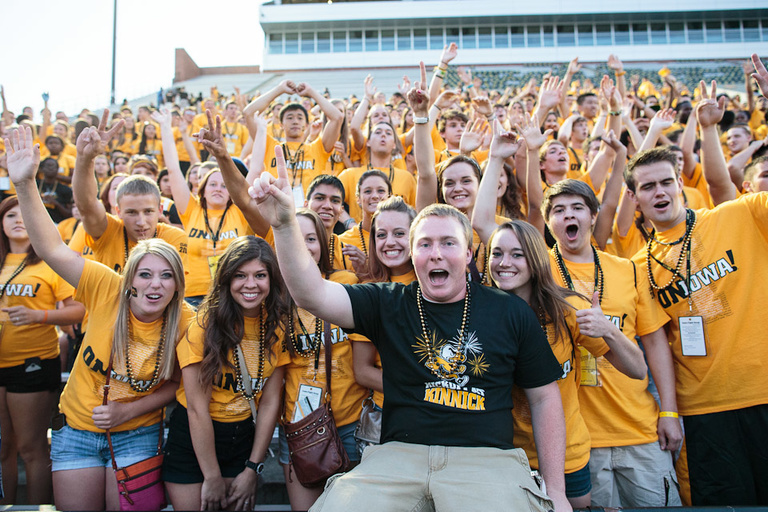  A man in a black t-shirt cheering with a group of people in yellow t-shirts in a football stadium.