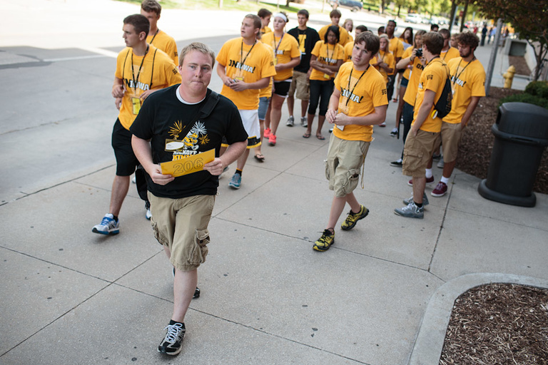 A man in a black-tshirt leading a group of people in yellow t-shirts down a sidewalk.