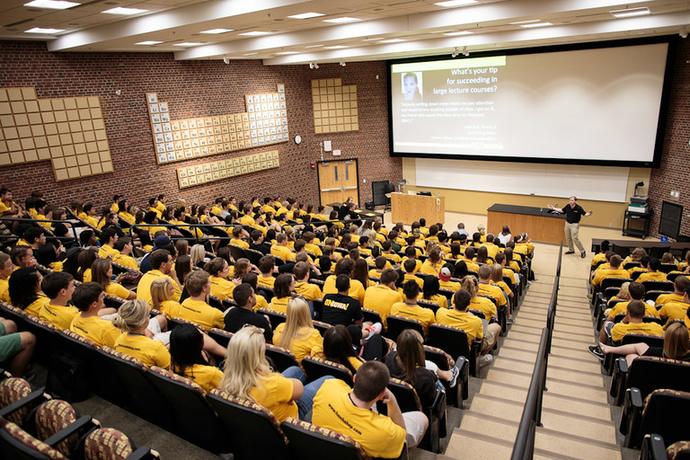 A lecture hall full of students in yellow t-shirts.