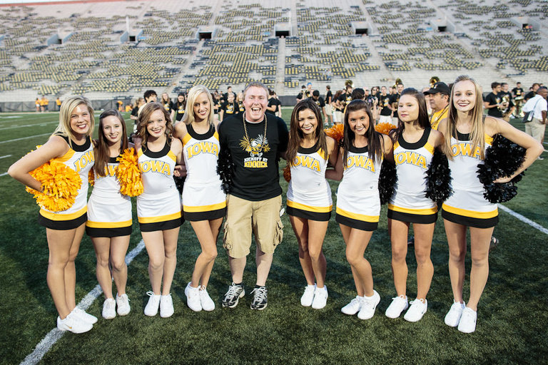 A man in a black t-shirt posing with a group of women cheerleaders.