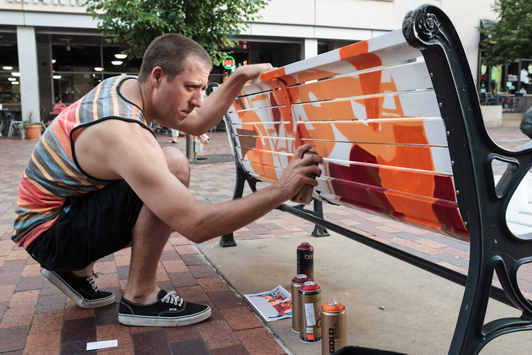 Man spray painting a bench.