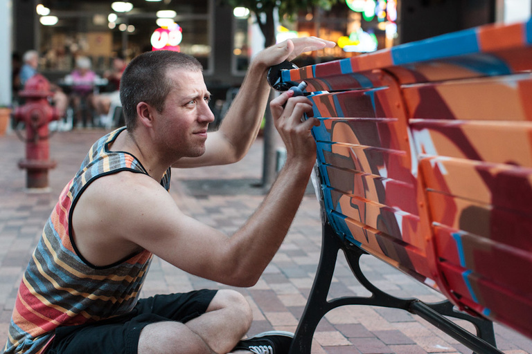 Man paints black lines on a bench in his spray paint design.