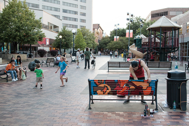 A man paints a bench while children run and play in his proximity.