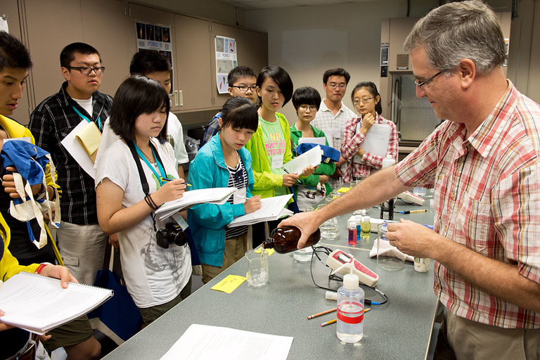 Doug Schoebelen pours river water into a beaker as a group of students listen to instructions for a water testing exercise