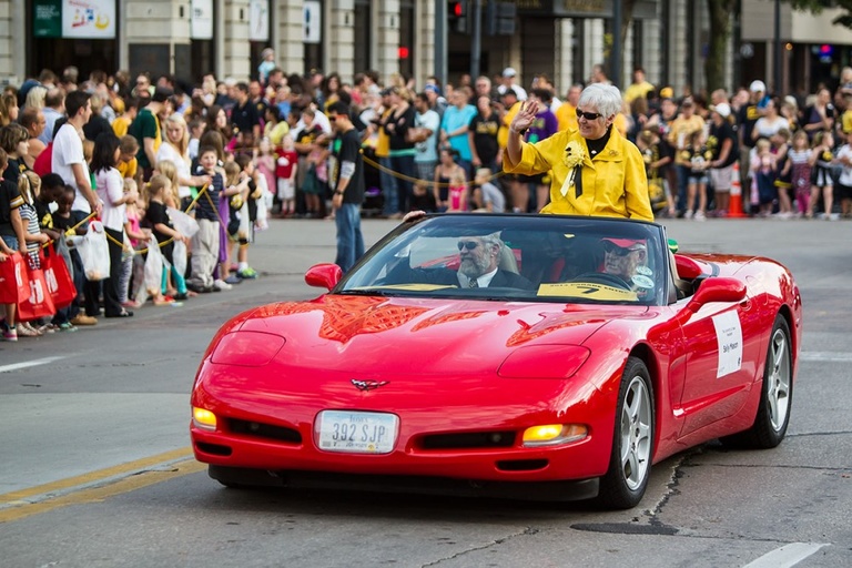 A woman in a yellow jacket riding on a red corvette in a parade.