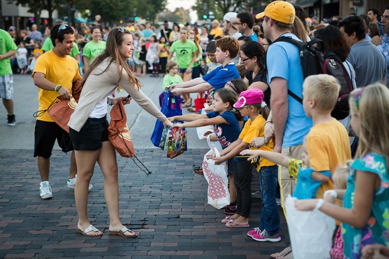 A girl gives candy to young children on a parade route.