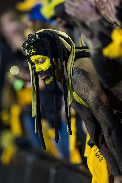 Fan in black and gold body paint leans over a railing.