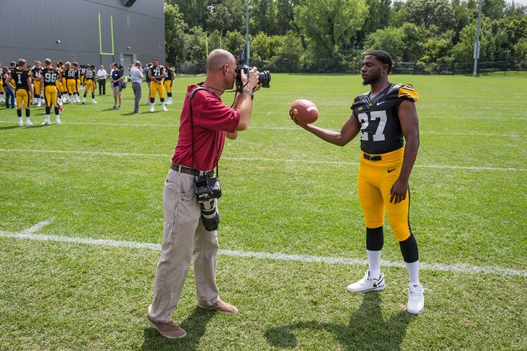 A photographer stands taking a photo of a football player in uniform.