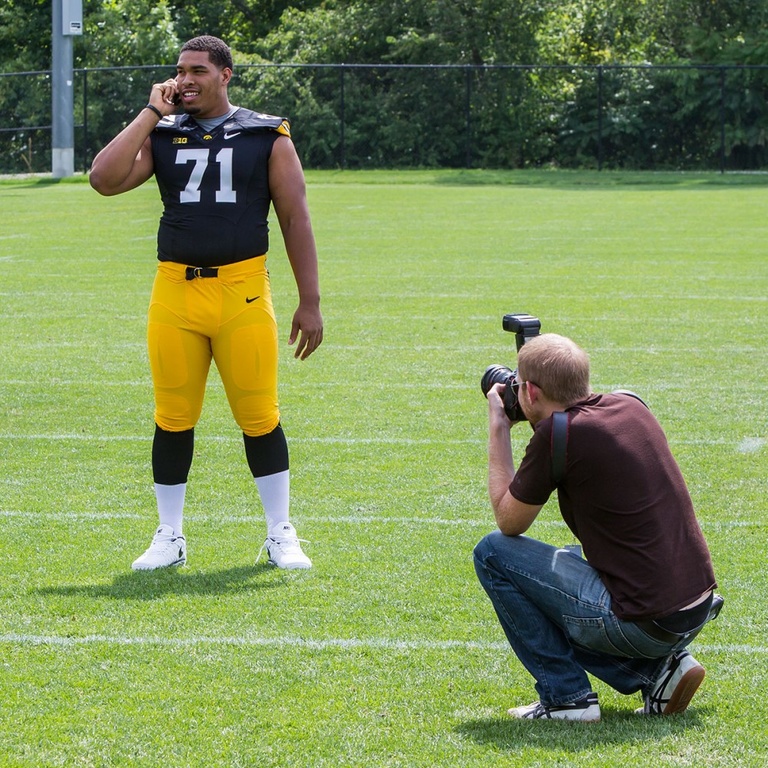 A photographer taking a photo of a football player who is talking on the phone.