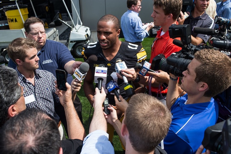 A football player addressing a group of reporters with microphones.