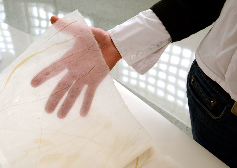 a woman's hand holds up a sheet of kozo paper, showing its transparency 