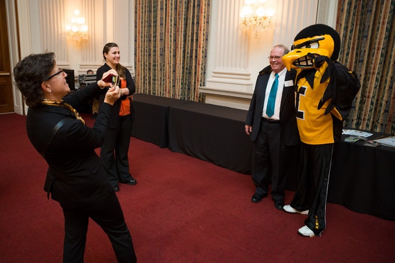 Jill Fishbaugh, director of strategic communications in the UI College of Education, snaps a photo of Herky as he poses with one of a steady stream of alumni and friends who stopped by for the Hawkeye Caucus event. 