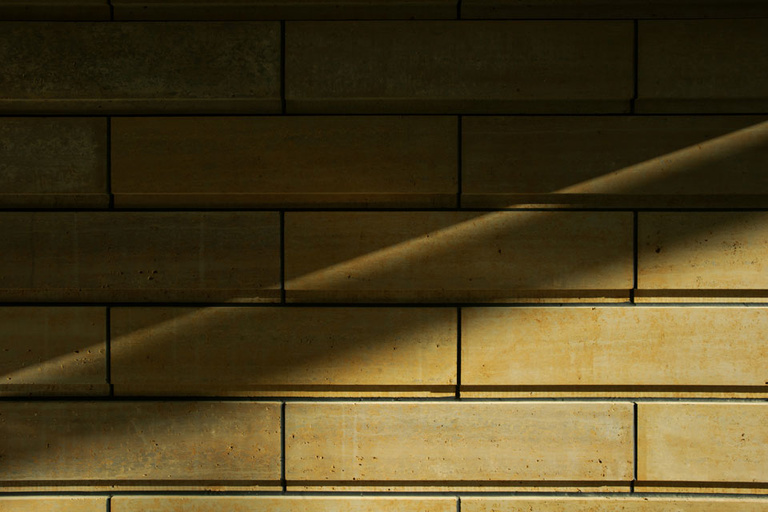 Light and shadow fall across a wall of limestone blocks