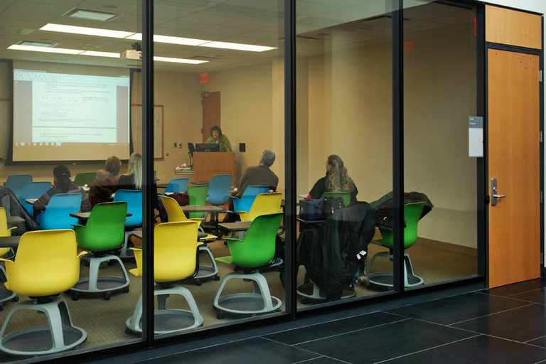 Class being taught in a room with brightly colored chairs.