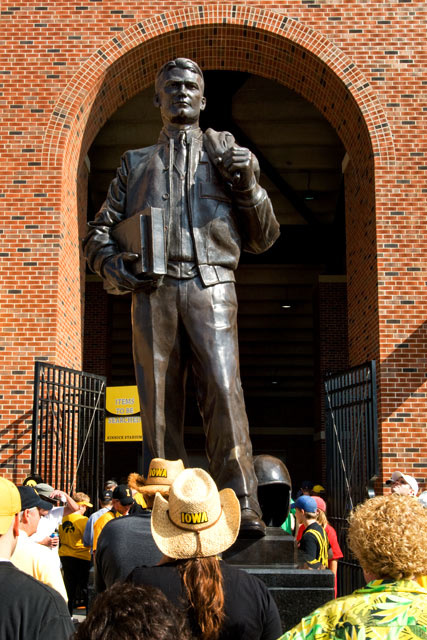 Color photo of football fans looking up at a bronze statue of Nile Kinnick