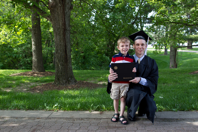 A UI graduate kneels beside his son.