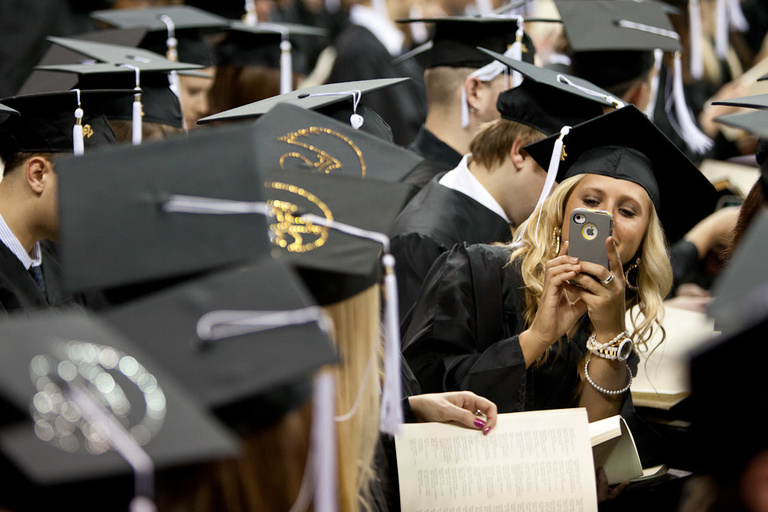 A graduate takes a photo of fellow grads with her phone.