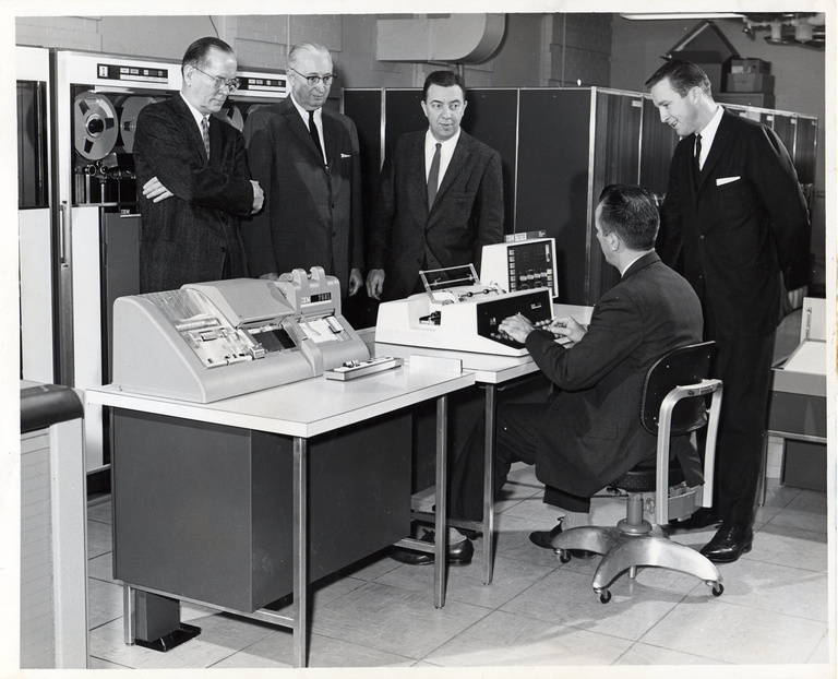 1961 black-and-white photo of computer center director demonstrating new IBM computers to four men