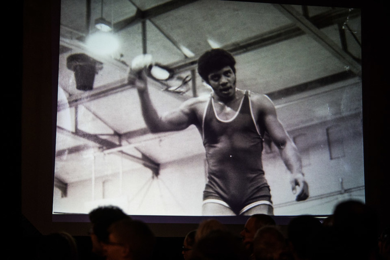 A black and white photo on a projector screen showing a man in a wrestling singlet.