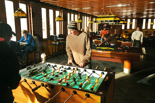 Color photo of students playing foosball and pool in the student union
