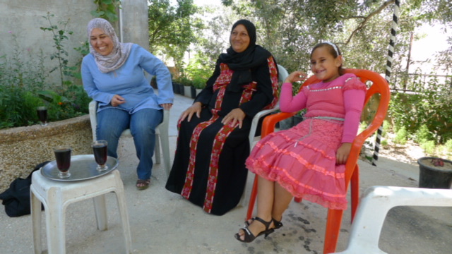 two women and a young girl in Palestine sit in chairs dressed in traditional clothing