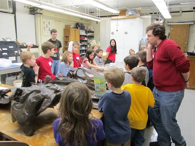 Children and adult supervisors look over replicas of dinosaur bones