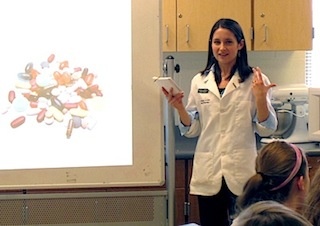Pharmacy student speaks to a class with photo of pills on the screen behind her.