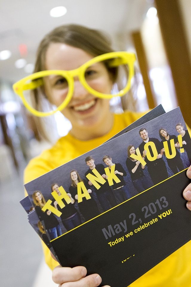 A student in oversized gold glasses holds up a sign that says "Thank You."
