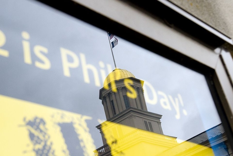 A banner announcing Phil's Day hangs in a window that also reflects the gold dome of the Old Capitol.
