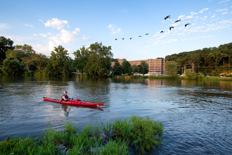 Canoe on river with geese and Mayflower Hall in background