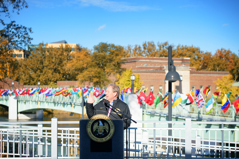 flags representing the home countries of university of iowa international students fly on the IMU footbridge; president bruce harreld speaking at ceremony