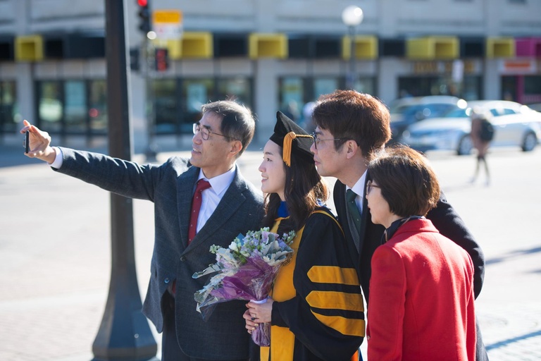 A graduate and their family take pictures on the Pentacrest. Photo by Tim Schoon.