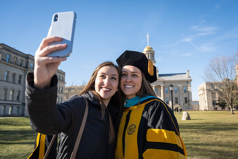 A graduate poses for a selfie on the Pentacrest. Photo by Tim Schoon.