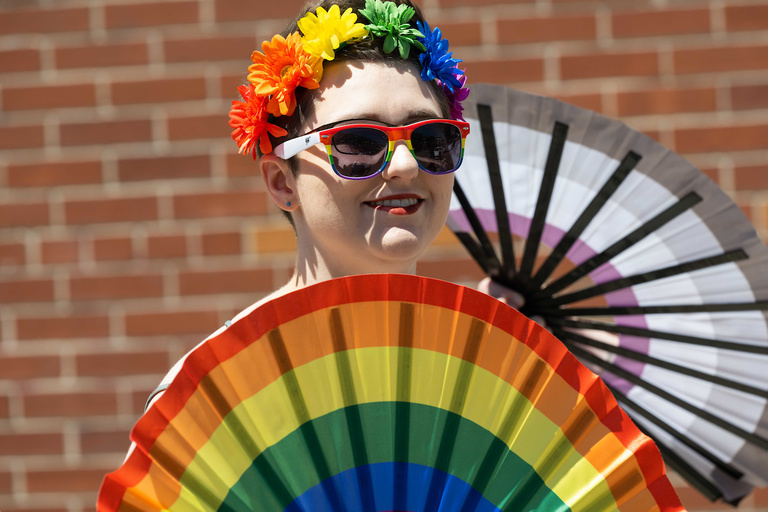 A parade attendee holding rainbow fans watches the parade.