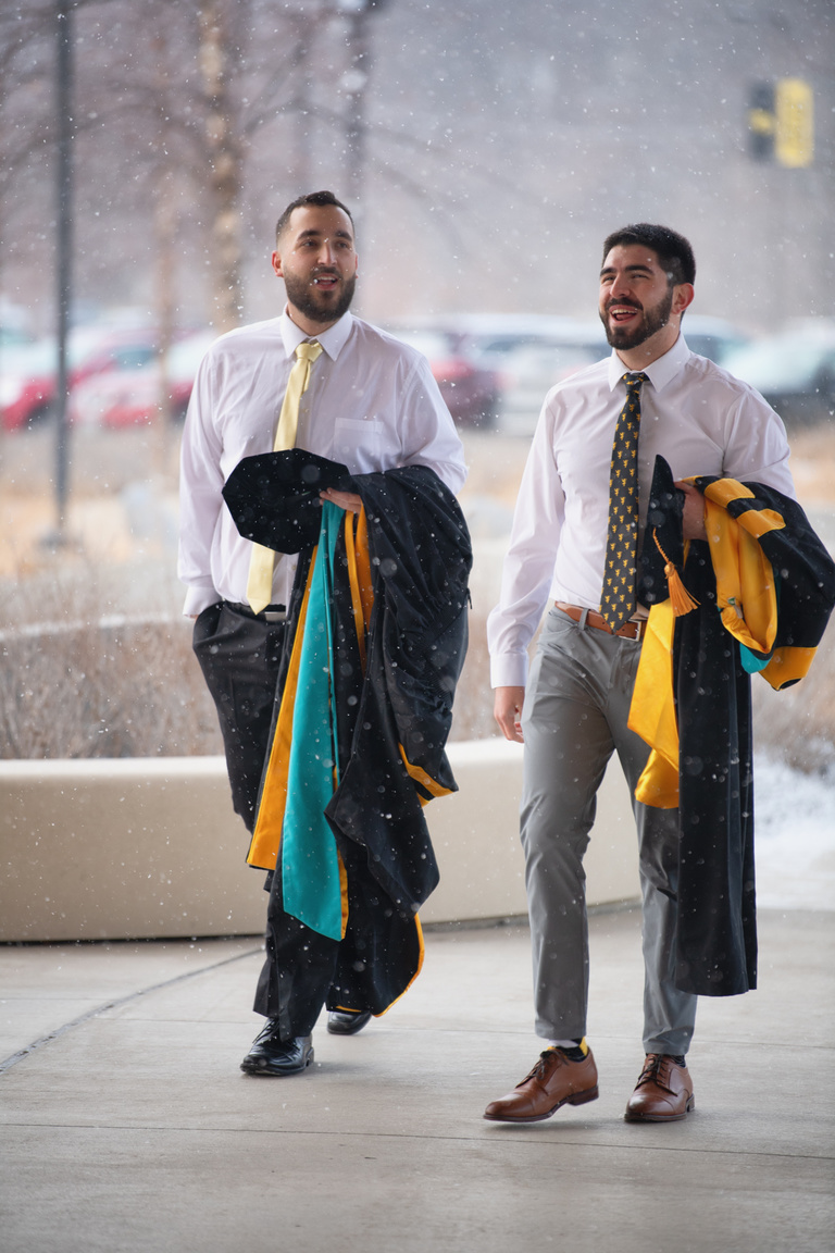 Snow flurries and Graduate College commencement. Two graduates arrive at Hancher Auditorium for the Doctoral Commencement Ceremony.