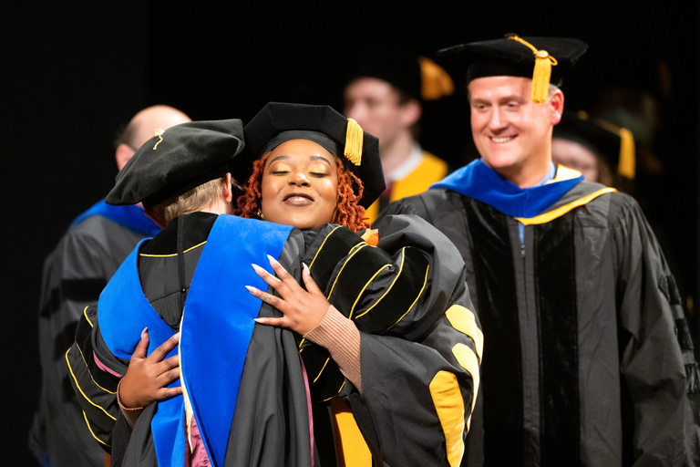 A student hugs a faculty member during the Graduate College's Doctoral Commencement Ceremony.