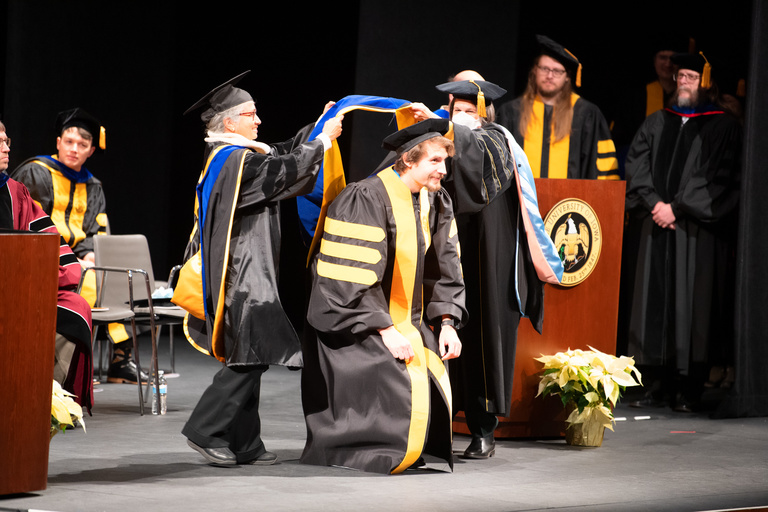 Doctoral regalia is placed upon a graduate during the Doctoral Commencement Ceremony on Friday, Dec. 16.