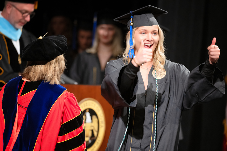 This student gives two thumbs up after receiving her diploma.