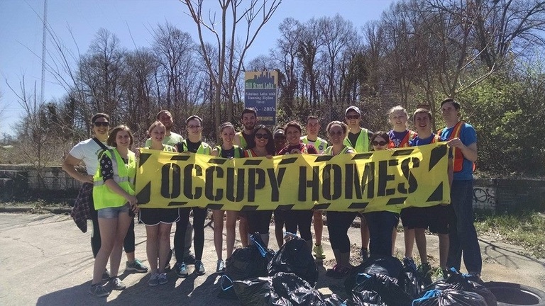 A group of students hold an "Occupy Homes" sign during a service learning project.