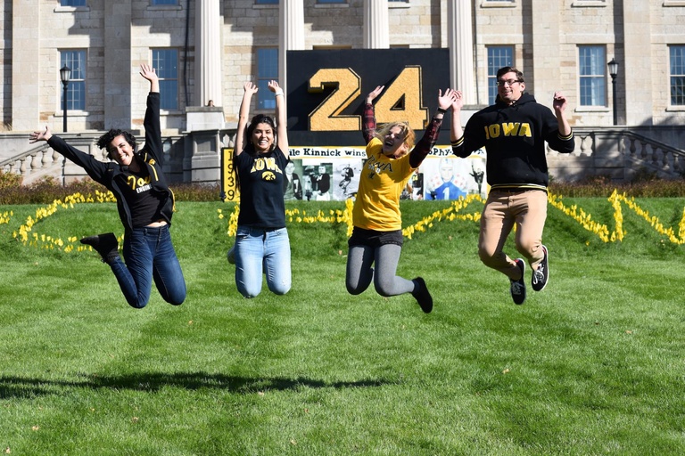 students jumping in front of 2019 corn monument on pentacrest